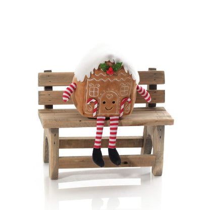 A fabric shelf sitter resembling a gingerbread house with a striped decoration, sitting on a wooden bench.