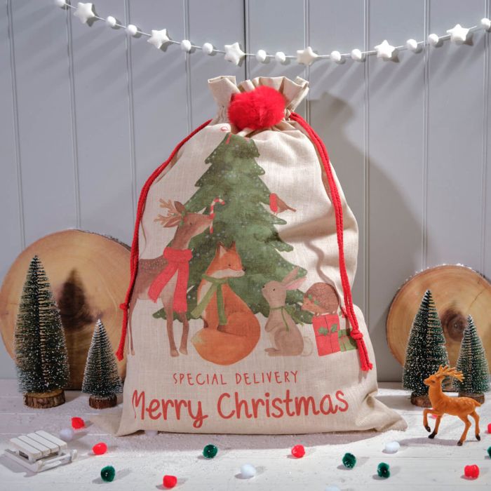 A beige Christmas sack with red trim and festive decorations, including a Christmas tree and reindeer, displayed on a wooden background with Christmas lights and small ornaments.