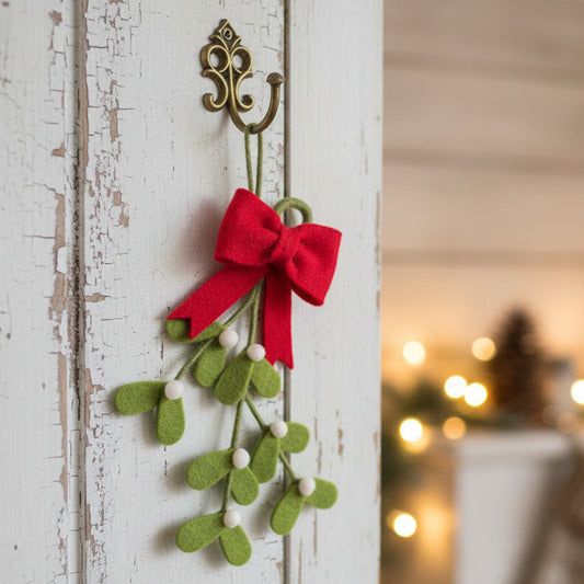 A felt Christmas mistletoe decoration with green leaves, small white berries, and a red felt bow, shown on a plain white background.