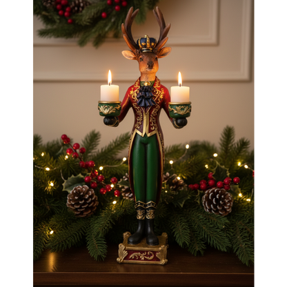 A festive Christmas stag candle holder figurine standing on a base, holding two lit white candles. The stag is dressed in a red and green military-style uniform with gold trim and a small gold crown.