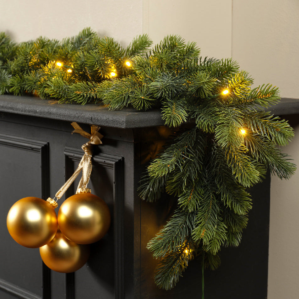 Decorative Christmas garland with lights and gold ornaments on a black surface.