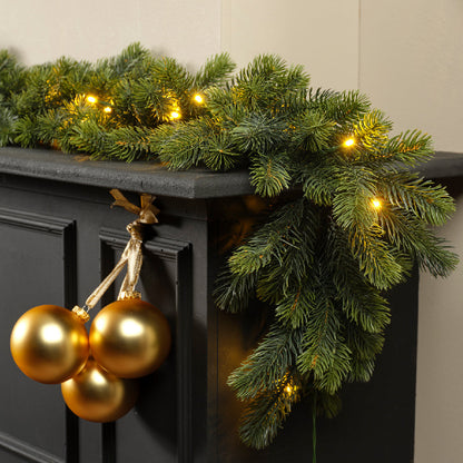 Decorative Christmas garland with lights and gold ornaments on a black surface.
