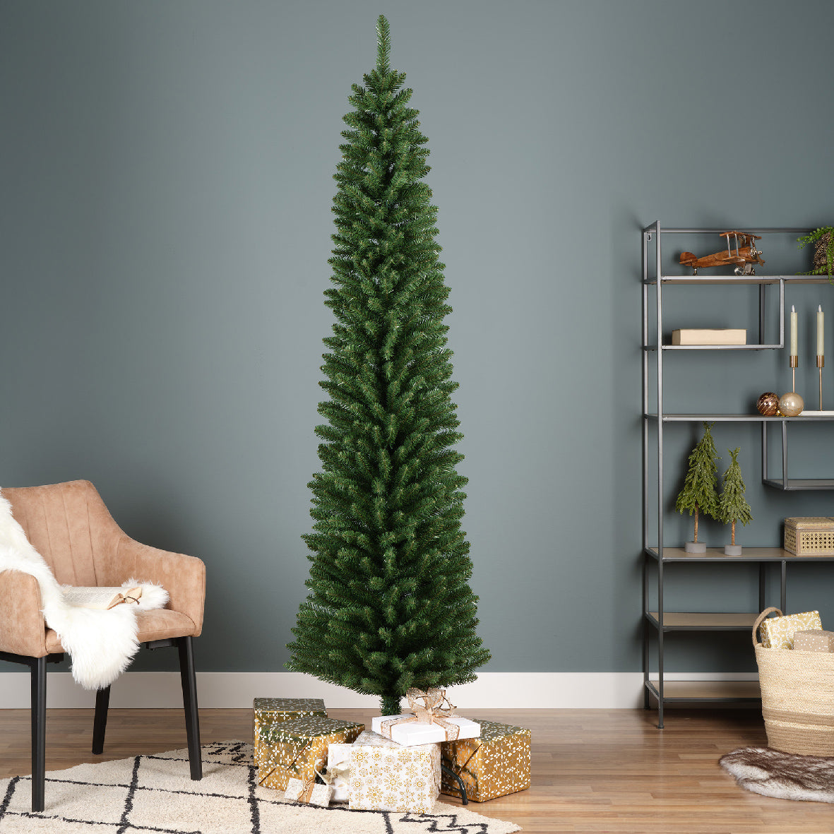 An artificial pencil pine Christmas tree with metal base, green in color, placed in a room with presents and decorations around it.