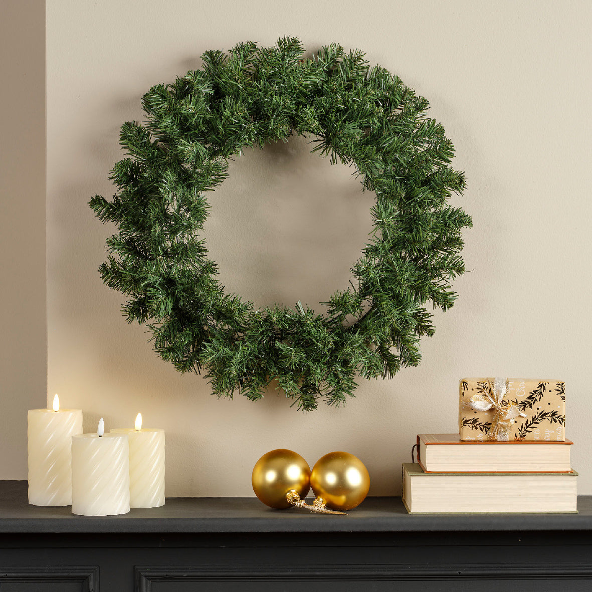 A round green Christmas wreath with soft needles, hanging on a doorway, accompanied by candles and decorative items.