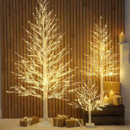 Three illuminated LED Christmas twig trees with berry lights with warm white glow, displayed in different sizes against a vertical wood-panelled wall with wrapped gifts at the base.