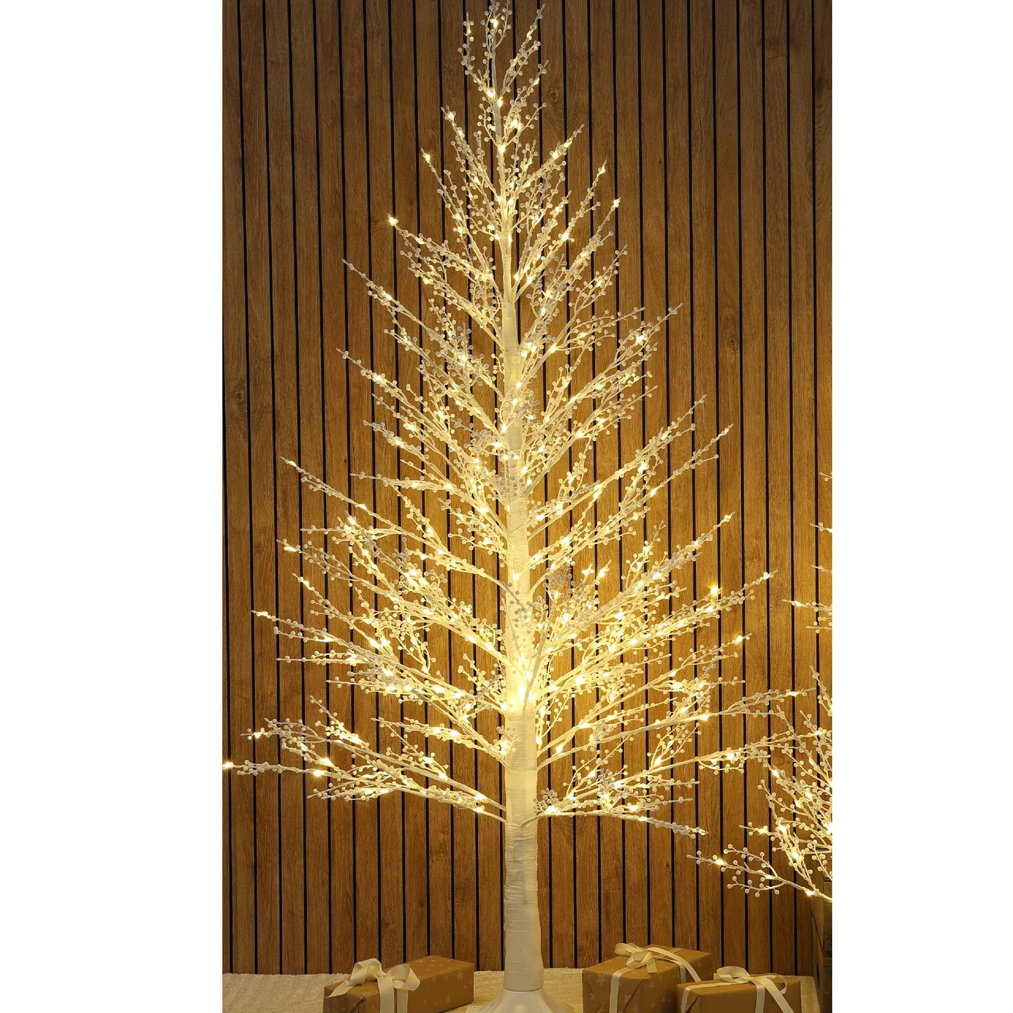 A decorative artificial tree with glowing warm white string lights, shown against a vertical brown wood plank wall with wrapped gifts at the base.