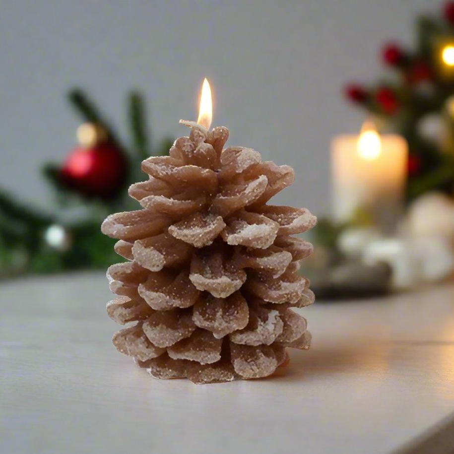 A rustic brown pinecone-shaped wax candle on a white surface, with a blurred warm light in the background, resembling a Christmas decoration.