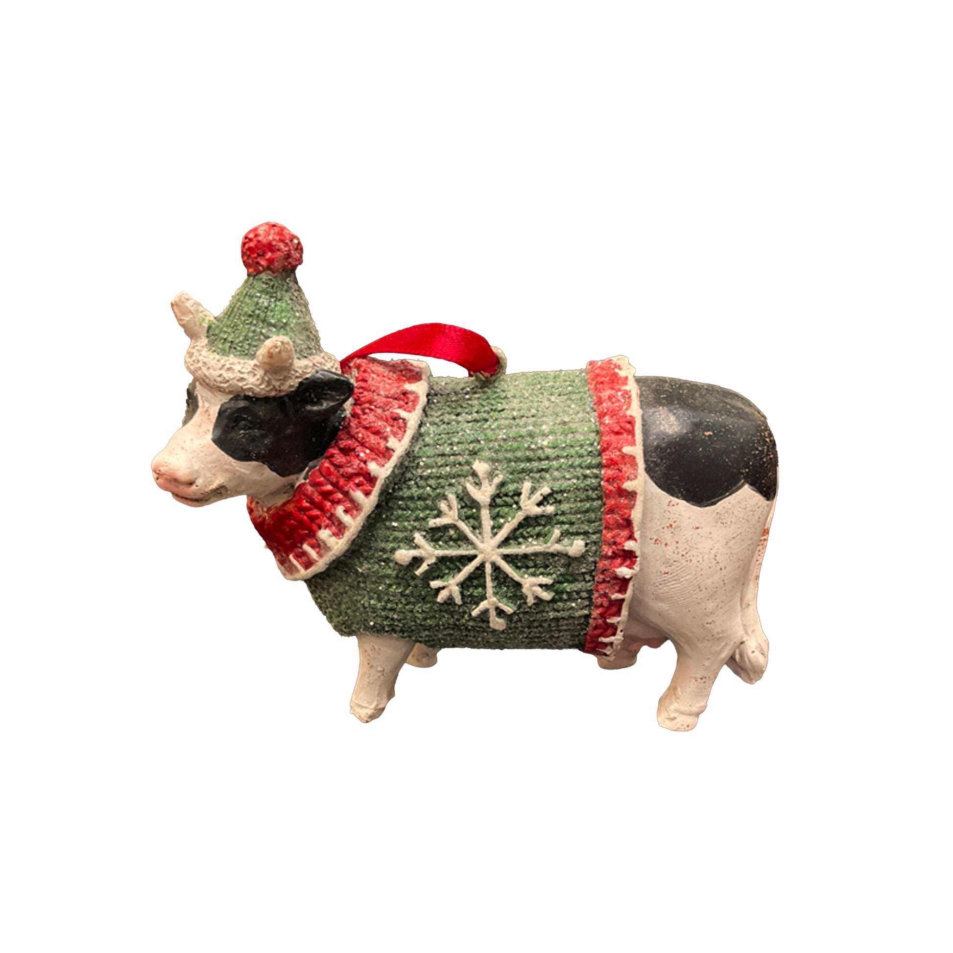 Small figurine of a cow wearing a green sweater with a snowflake design, red scarf, and green hat on a white background.