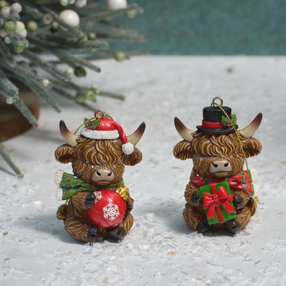 Two small Highland cow Christmas ornaments on a snowy white surface. One ornament wears a Santa hat and green scarf while holding a red ornament, and the other wears a black top hat with a red bow and green gift while holding a wrapped present.