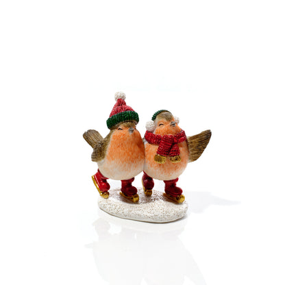 A small decorative figurine of two birds dressed in festive clothing, standing on a glittery white base against a plain white background.