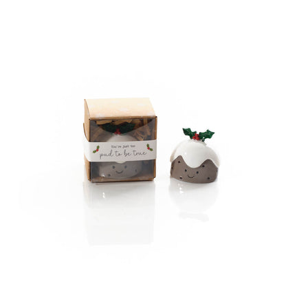 A small ceramic Christmas pudding figurine with white icing, brown body, and a green holly sprig, shown next to its clear windowed gift box with a white paper label.