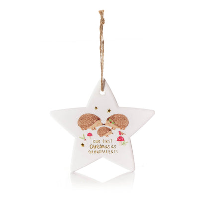A white five-pointed star Christmas ornament with a hanging twine loop, featuring an illustration of three hedgehogs and the text 'OUR FIRST Christmas as GRANDPARENTS' on a clean white background.