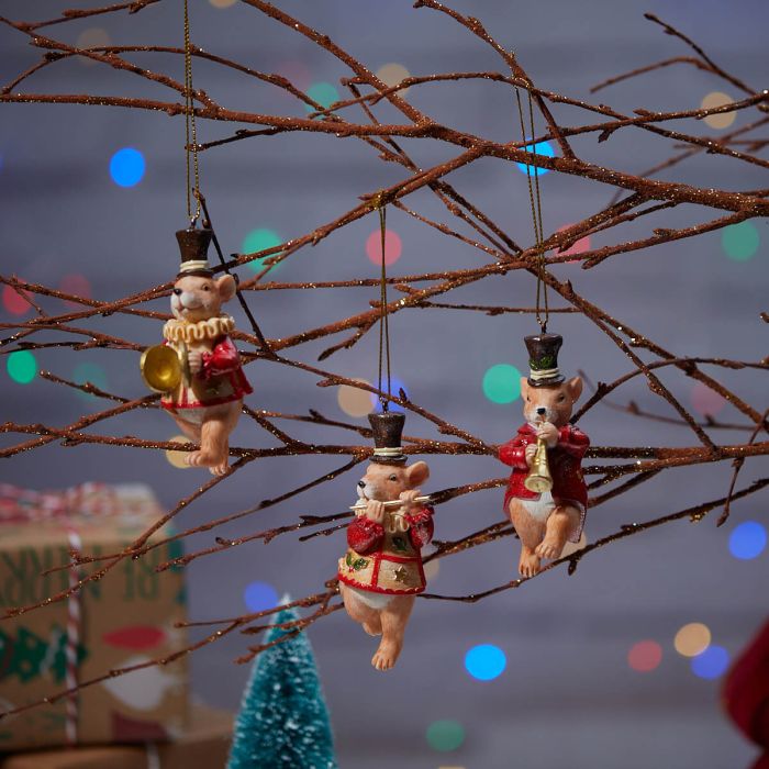 Three polyresin mouse hangers in festive attire, hanging from branches with a blurred Christmas tree in the background.