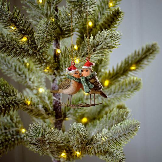 A decorative Christmas ornament featuring two robins perched on a branch with a festive bow and leaves, hanging on a Christmas tree.