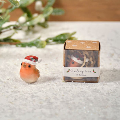 A small resin robin keepsake ornament wearing a Santa hat, displayed next to its packaging which has 'Sending Love' written on it.
