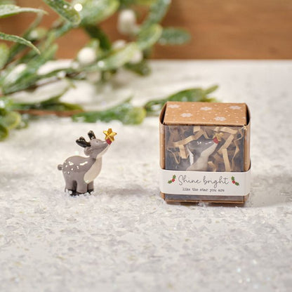 A small resin reindeer ornament with a golden holly leaf on its head, displayed next to its packaging which has 'Shine bright' text.