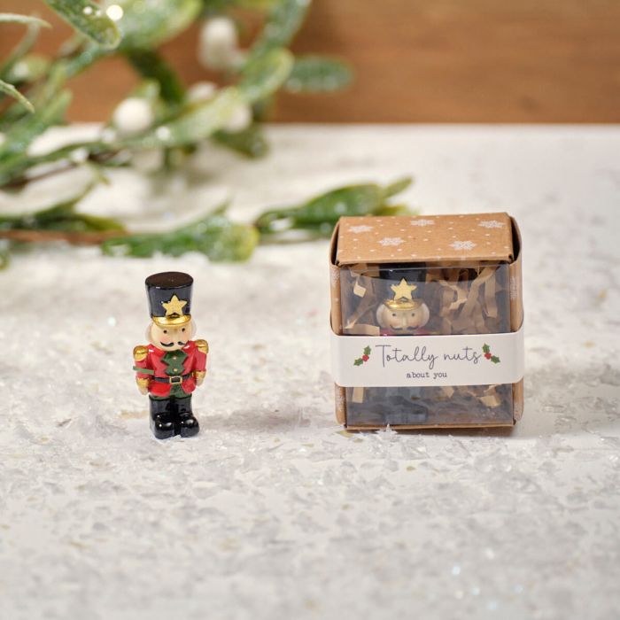 A small resin nutcracker keepsake ornament next to its packaging, which is decorated with a Christmas-themed design.