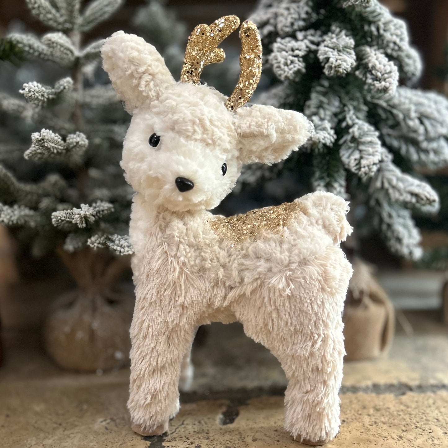 Plush deer toy with gold antlers in front of a Christmas tree.