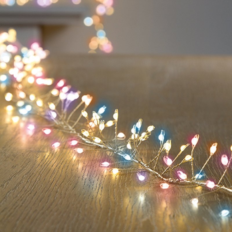 Rainbow fairy cluster pin lights draped across a wooden floor, casting a warm glow with soft bokeh light reflections in the background.