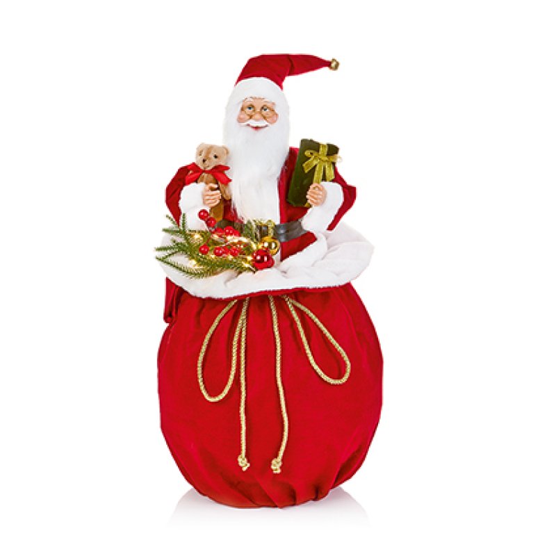A festive Santa Claus holiday decoration featuring a seated Santa in a red suit and hat with a white beard, holding a sack filled with gifts, evergreen branches, and red berries, photographed on a clean white background.