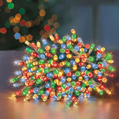 Multicolor Christmas string lights with many small round bulbs in red, green, blue, yellow, and white, clustered on a tabletop with a blurred holiday background.
