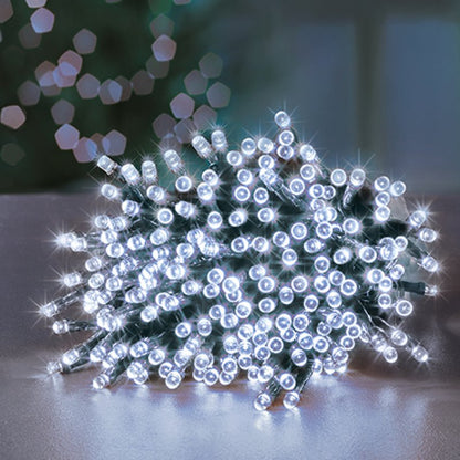 A pile of white LED fairy string lights glowing brightly on a reflective surface, with a softly blurred holiday background.