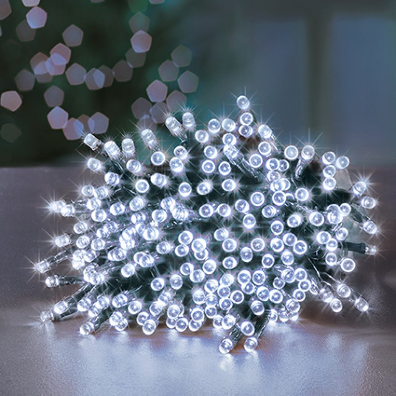 A pile of white LED fairy string lights glowing brightly on a reflective surface, with a softly blurred holiday background.