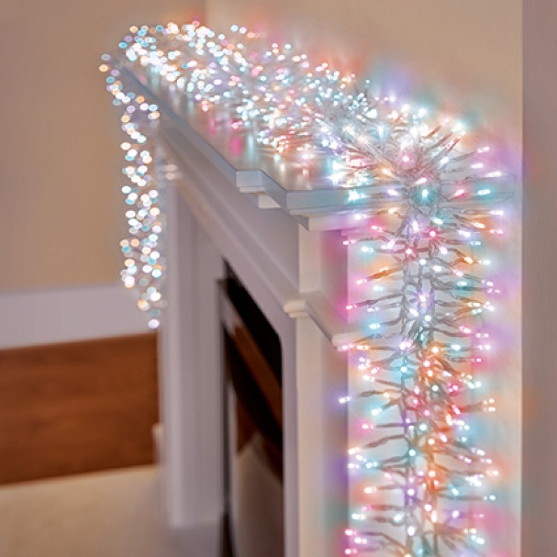rainbow Christmas string lights with clear cable draped over a white fireplace mantel in a cosy indoor setting.