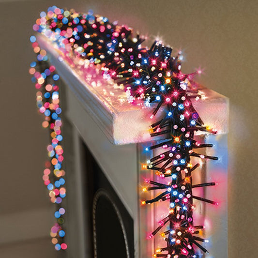 Christmas garland with rainbow string lights draped over a fireplace mantel, casting colourful  light reflections.