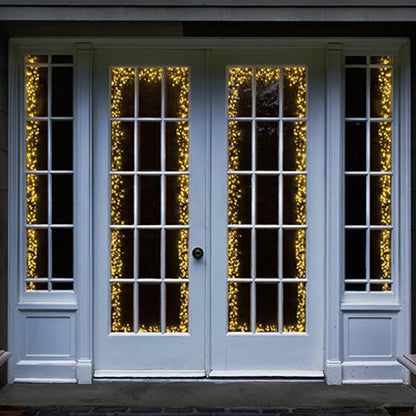 White French door and side panels with vintage gold string lights draped vertically along the glass panes, set against a dark background.