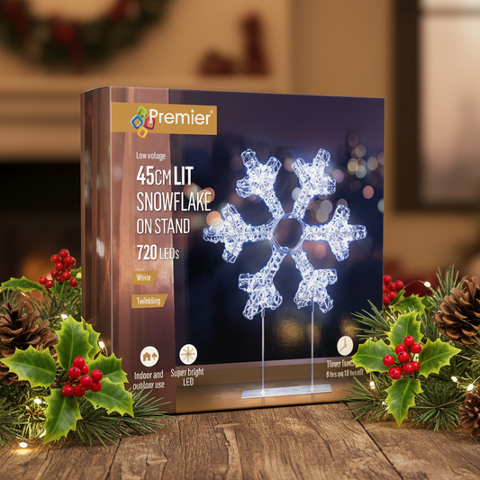 Premier 45cm LED snowflake light on a stand, shown in its retail packaging box surrounded by festive holly and pine branches on a wooden surface.