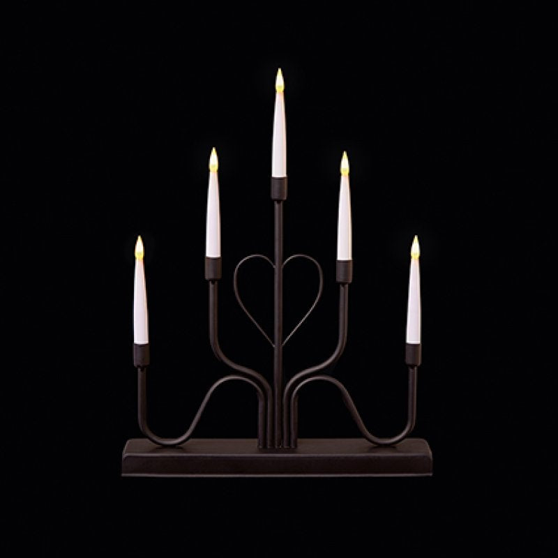 A six-light candle-style candelabra with a dark metal frame and five white faux candles, each lit with a warm yellow flame, set against a solid black background.
