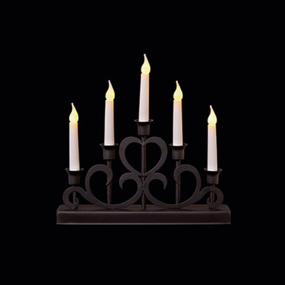 A five-light candle-style table lamp with a dark metal scrollwork base and five white faux candles, each lit with a warm yellow flame effect, shown against a solid black background.
