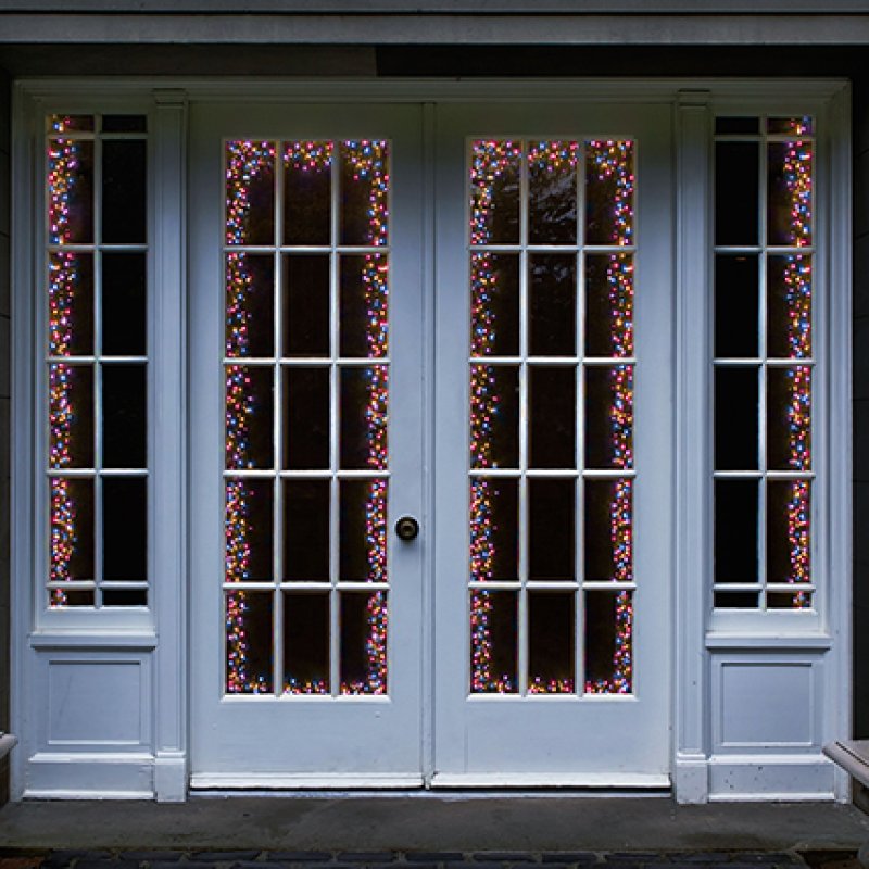 White French door double set with decorative rainbow Christmas string lights draped vertically in the glass panes, set against a dark background.
