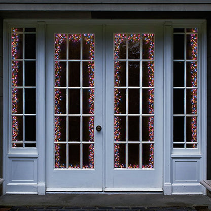 White French door double set with decorative rainbow Christmas string lights draped vertically in the glass panes, set against a dark background.