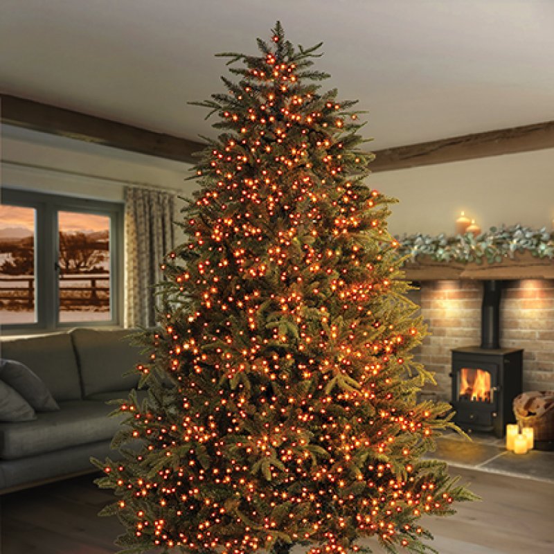 A tall artificial Christmas tree with vintage gold led lights, standing in a cosy living room with a fireplace and sofa in the background.