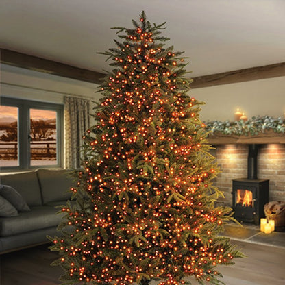 A tall artificial Christmas tree with vintage gold led lights, standing in a cosy living room with a fireplace and sofa in the background.