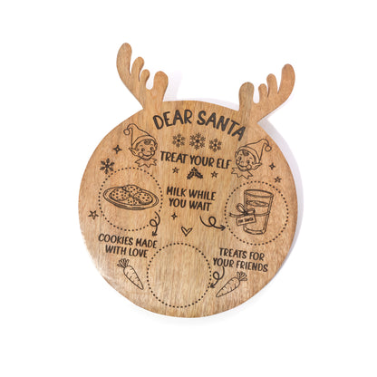 A round wooden cutting board designed to look like Santa's reindeer head, featuring engraved holiday illustrations and the text 'DEAR SANTA TREAT YOUR ELF, MILK WHILE YOU WAIT, COOKIES MADE WITH LOVE, TREATS FOR YOUR FRIENDS'.