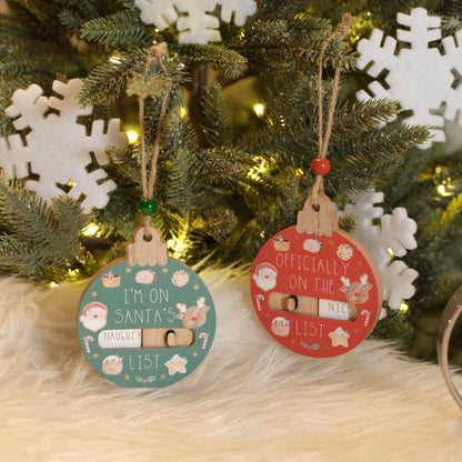 Two Christmas naughty and nice Christmas tree ornaments with humorous text in front of a decorated Christmas tree.