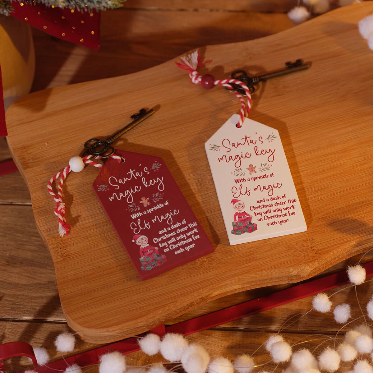 Two Christmas-themed hanging tags with antique-style keys and red-and-white twisted cord, displayed on a wooden board with festive props.