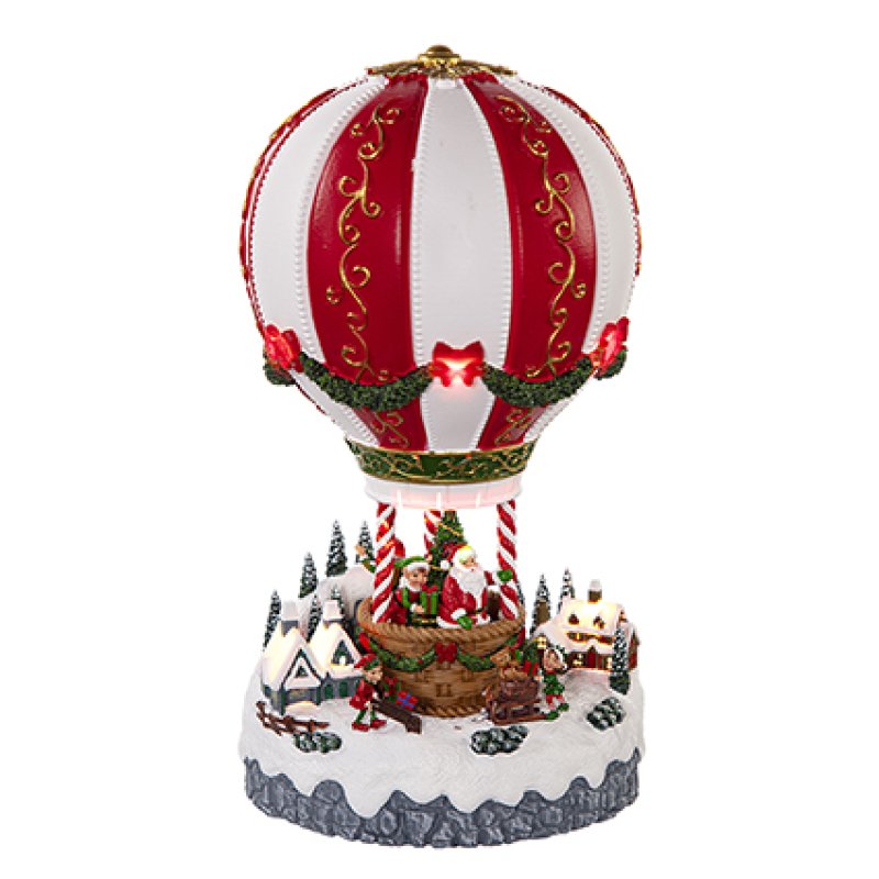 A festive Christmas hot air balloon figurine with red and white striped balloons, gold scrollwork, green garlands with red bows, Santa in a basket, and a snowy village scene on a white background.