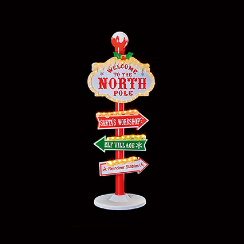 A decorative Christmas-themed North Pole signpost with multiple directional lights and signs reading 'Welcome to the North Pole,' 'Santa's Workshop,' 'Elf Village,' and 'Reindeer Stables' shown on a solid black background.
