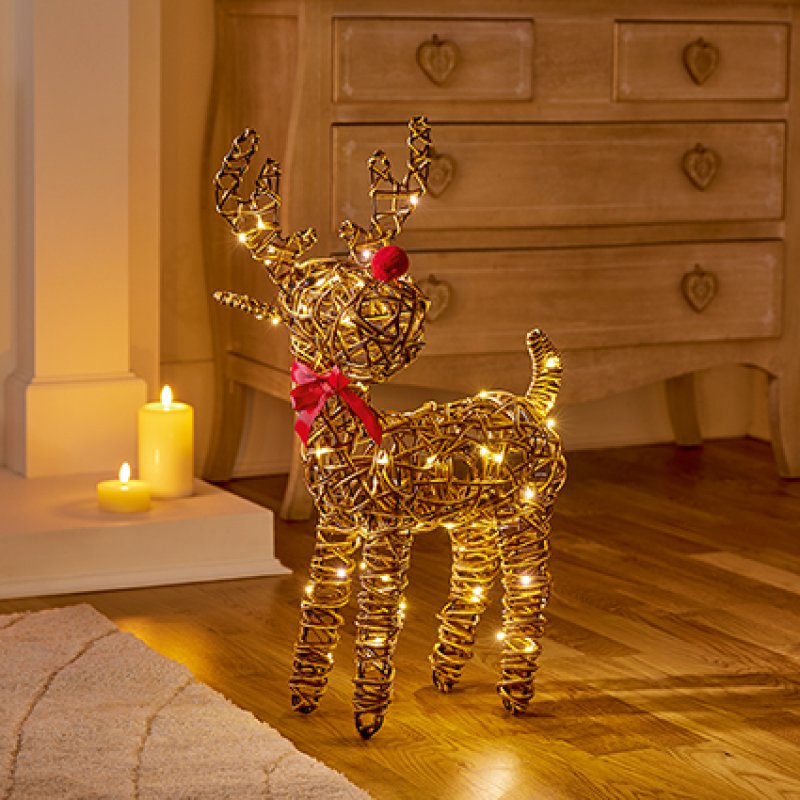 Decorative wicker reindeer with lights on a wooden floor next to candles.