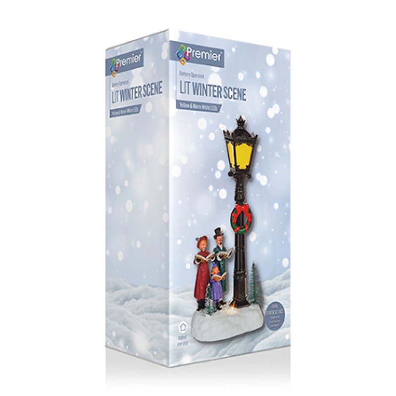 Premier Lighting 'Lit Winter Scene' decorative lamp post set in its retail packaging, featuring a black lamp post with a glowing yellow lantern, a red wreath, and two small holiday figures under falling snow graphics.