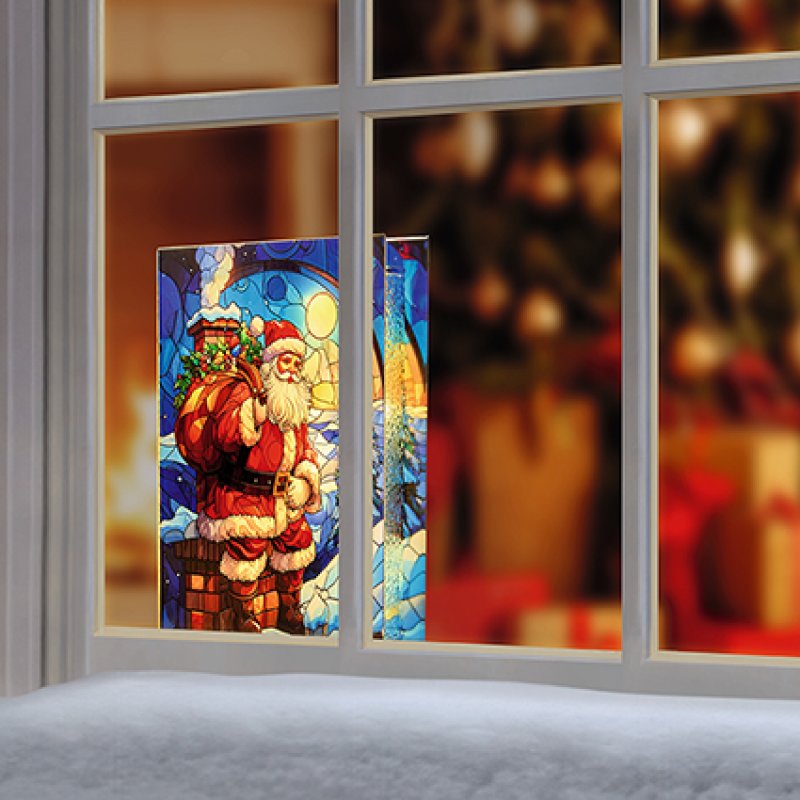 A Christmas-themed stained glass window panel featuring Santa Claus, shown installed on a white-framed window with a warm, festive interior blurred in the background.