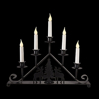 A black metal 5-light candelabra with a triangular frame, featuring silhouettes of deer and a Christmas tree on the front, holding five white faux candles with lit flame tips, set against a solid black background.