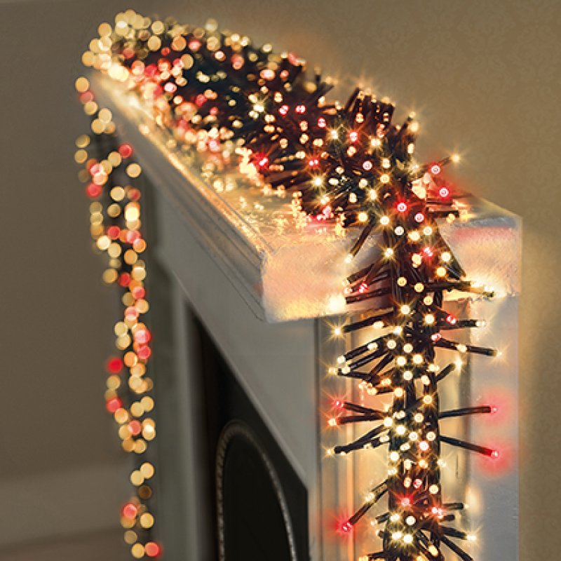 Christmas cluster lights with warm white and red lights draped over a fireplace mantel, with the garland also hanging down the left side.
