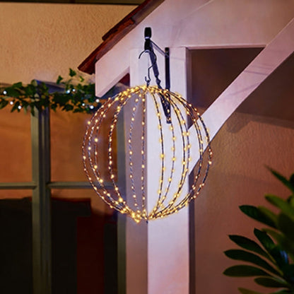 A spherical metal hanging light fixture filled with warm white LED fairy lights, suspended from a white porch beam at night.
