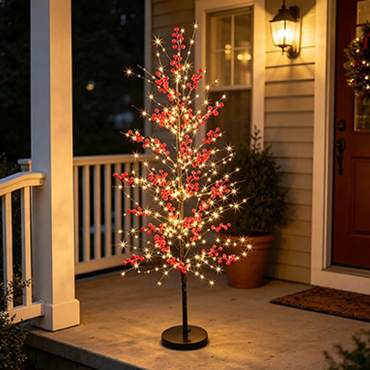 A small artificial Christmas tree with red berries and warm white string lights on a black stand, displayed on a front porch at night.