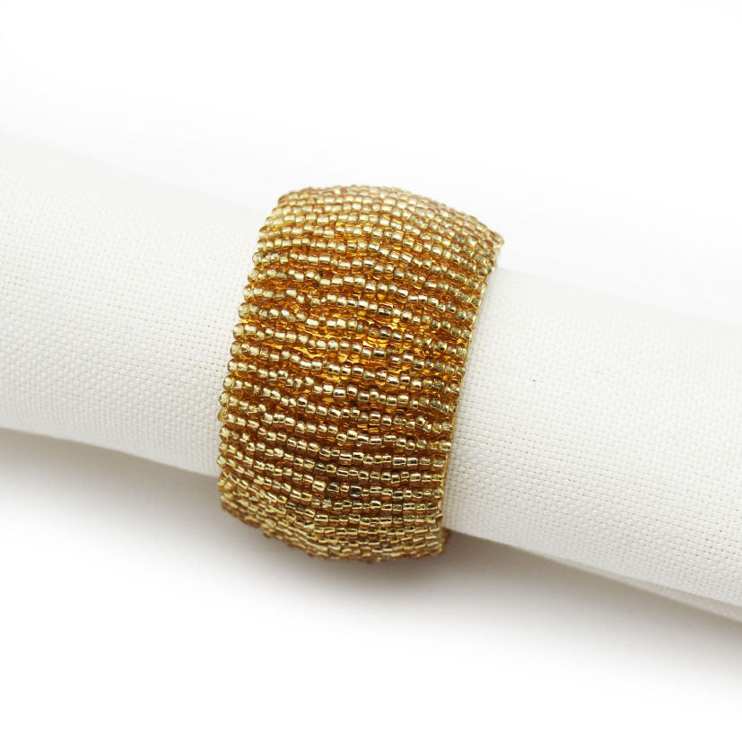A wide, chunky gold bead napkin ring displayed on a white fabric napkin against a white background.